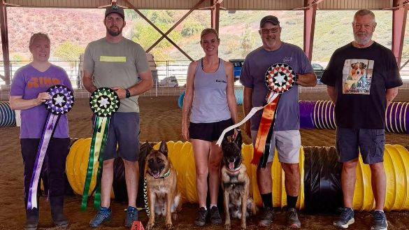 Several winners of the June 2026 NADAC Trial in Norco, CA posing with their ribbons and their dogs.